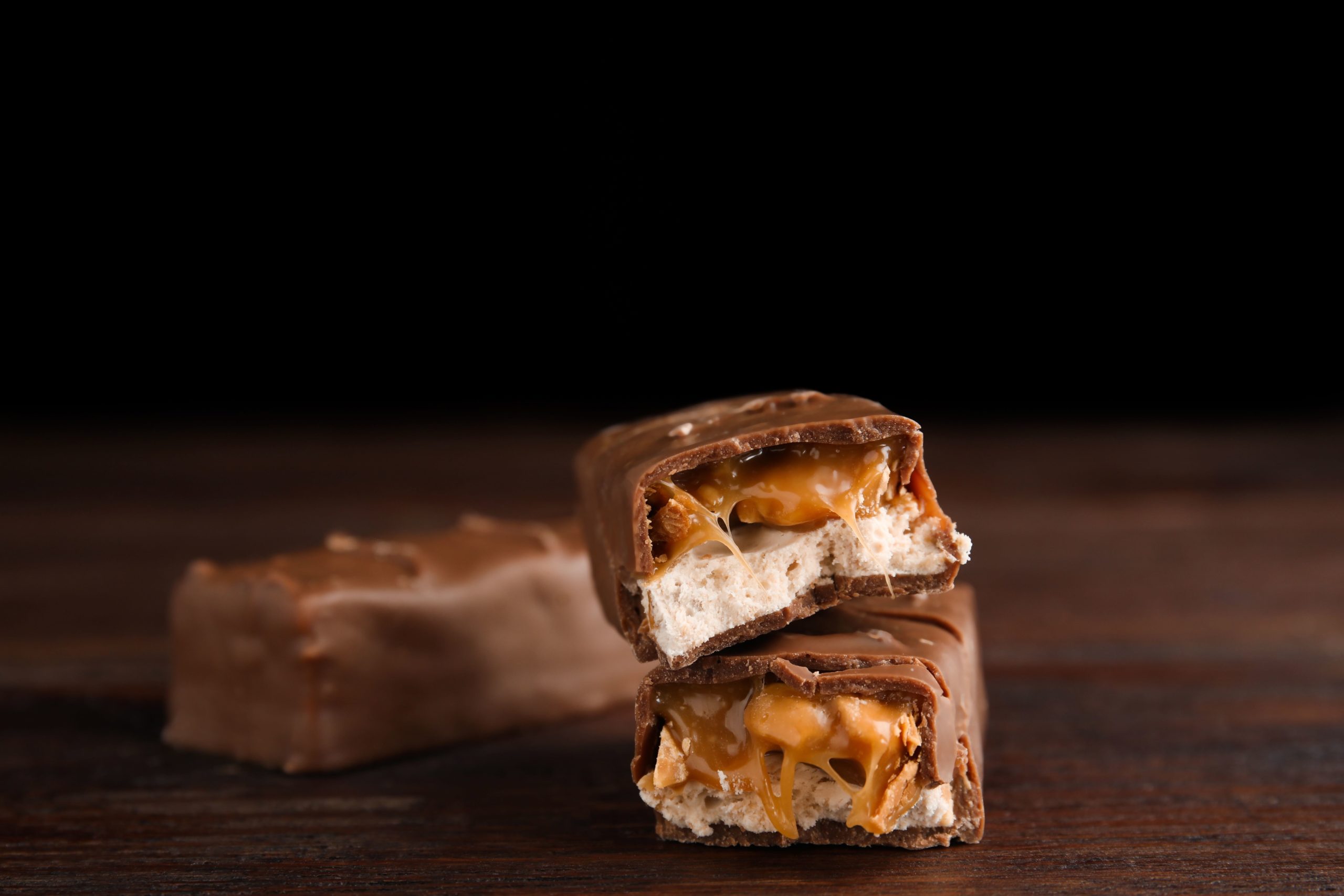 Chocolate bars with caramel, nuts and nougat on wooden table, closeup